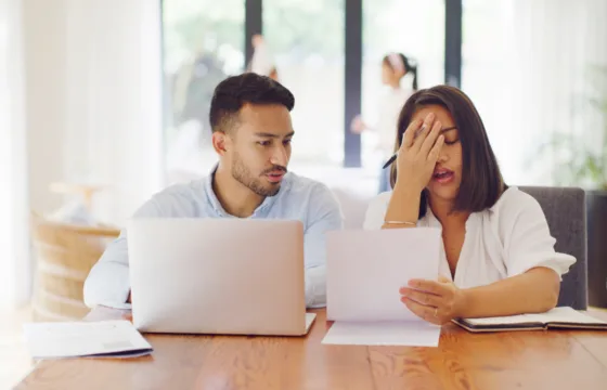 A Brief Overview Of Chapter 13 Bankruptcy Two people sit at a table with laptops and documents; one looks concerned while the other holds her head and a paper, appearing stressed—likely discussing the challenging details of filing for Chapter 13 bankruptcy in Iowa.